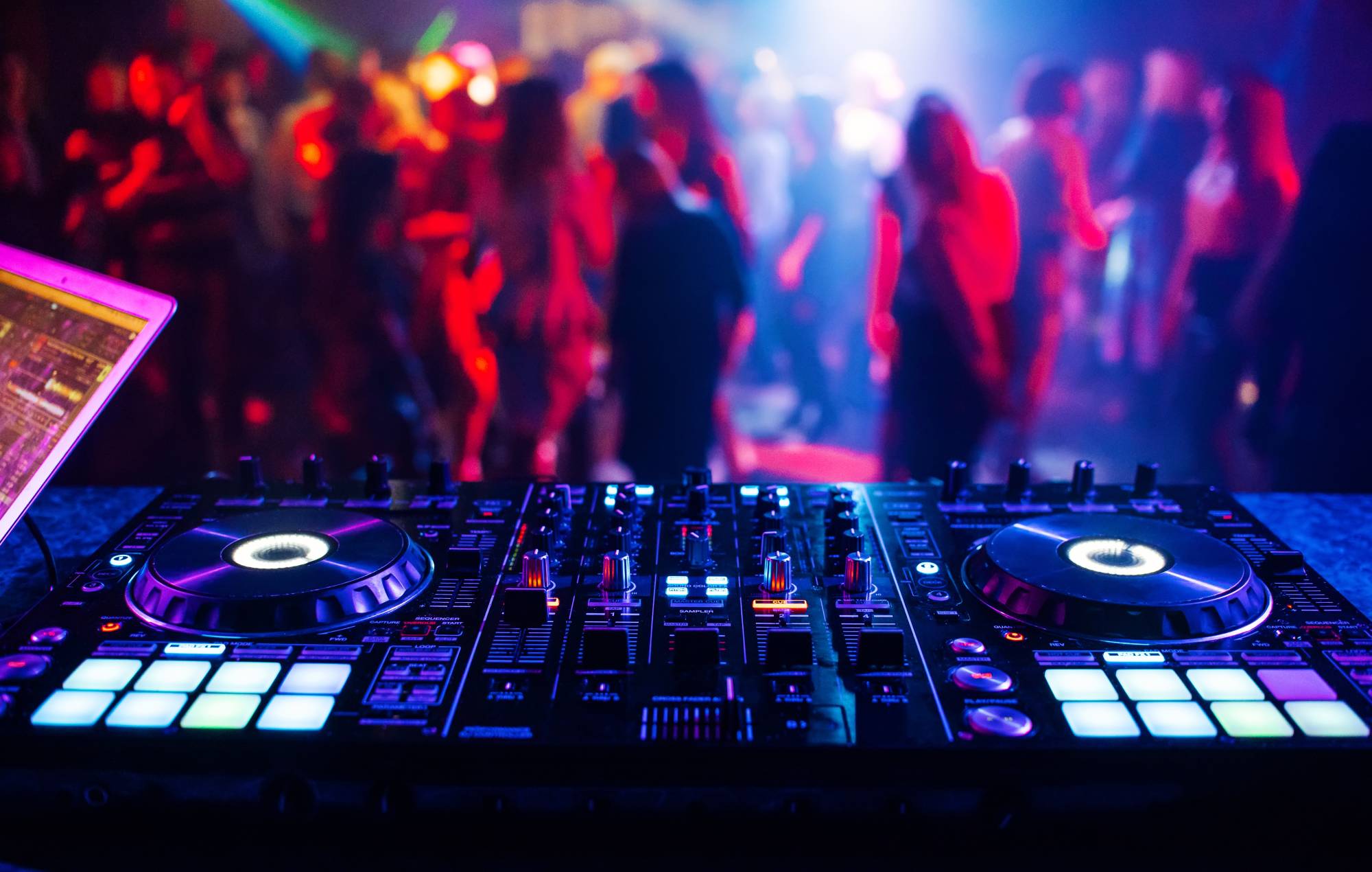 DJ Mixer Musical Controller at a nightclub at a party with blurry silhouettes of dancing people. Credit: Alex Coral via Getty